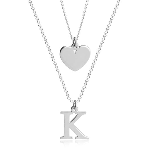 A stylish heart initial layered necklace featuring two delicate chains, each with its own charm. One chain showcases a small heart pendant, while the other displays a personalized initial charm, creating a meaningful and fashionable combination. 